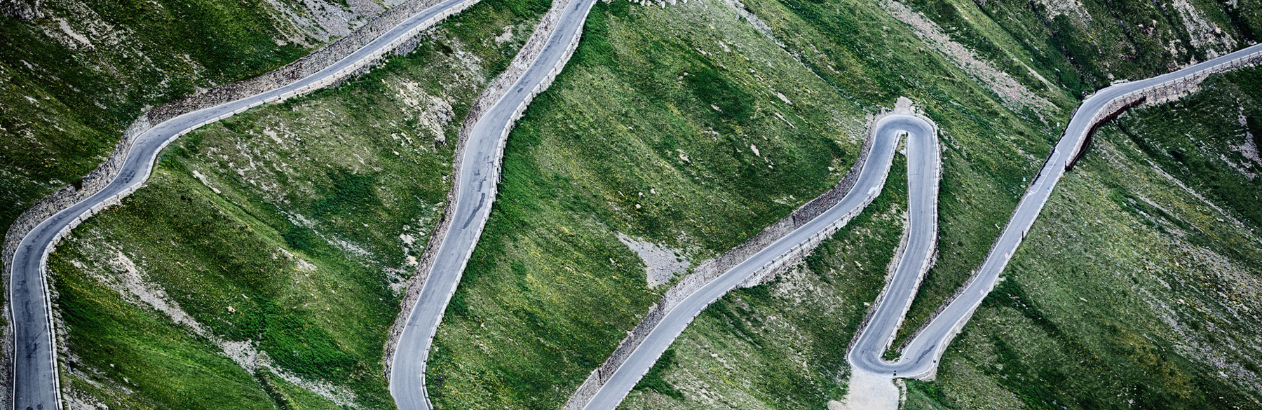 Luftaufnahme einer kurvigen Straße, die durch eine grüne, bergige Landschaft führt.